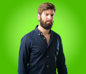 Obraz premium Young hipster man with big beard irritated and angry expressing negative emotion, annoyed with someone over green background