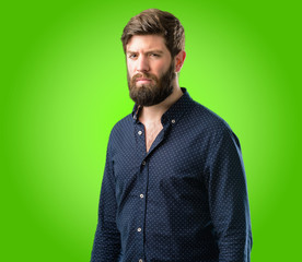 Young hipster man with big beard irritated and angry expressing negative emotion, annoyed with someone over green background