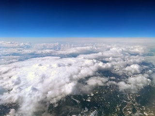 high altitude view of the earth from an airplane with deep blue sky and clouds covering a mountain landscape
