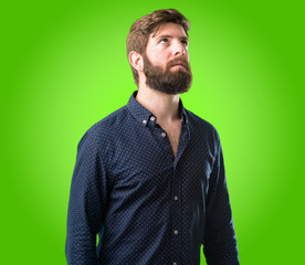 Young hipster man with big beard confident and happy with a big natural smile laughing looking up over green background