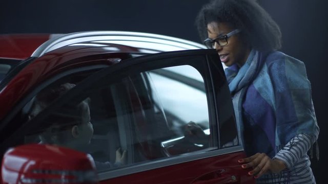 Content African-American woman with boy exploring shiny red car making purchase in car showroom.