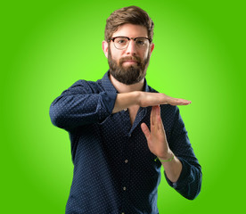 Young hipster man with big beard serious making a time out gesture with hands over green background