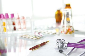 closeup of the desk of a doctors office with a stethoscope in the foreground and a bottle with pills in the background