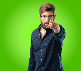 Young hipster man with big beard pointing to the front with finger over green background