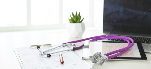 closeup of the desk of a doctors office with a stethoscope in the foreground and a bottle with pills in the background