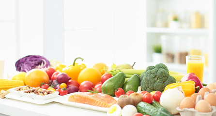 happy young housewife sitting in the kitchen preparing food from a pile of diverse fresh organic fruits and vegetables