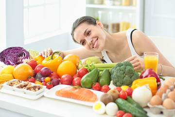 happy young housewife sitting in the kitchen preparing food from a pile of diverse fresh organic fruits and vegetables