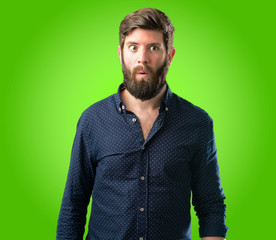 Fototapeta premium Young hipster man with big beard happy and surprised cheering expressing wow gesture over green background