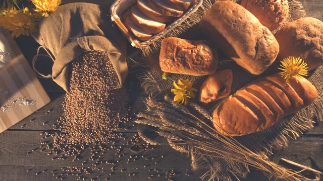 Still life with bread, wheat, flour and flowers.
Top view. Horizontal ( from left to right ) pan.
Ears of wheat, bank with flour, a bag of grain and bread are on an old wooden table.