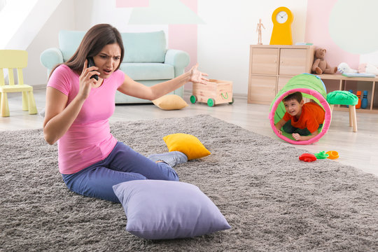 Playful little boy and annoyed nanny talking on phone at home