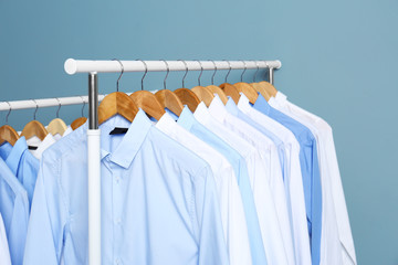 Racks with clean clothes after dry-cleaning against color background