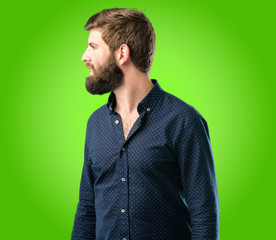 Young hipster man with big beard side view portrait over green background