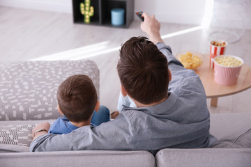 Young man watching TV with his son on sofa at home