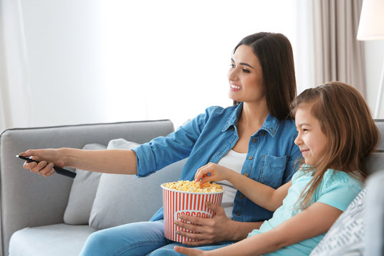 Young woman watching TV with her daughter on sofa at home