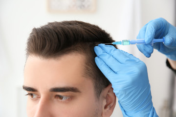 Naklejka premium Young man with hair loss problem receiving injection on blurred background, closeup