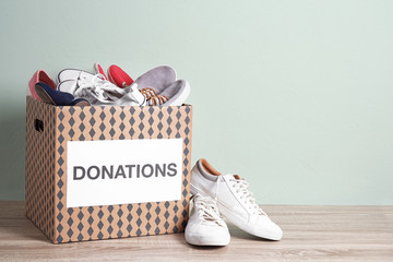 Donation box with shoes on wooden table against color background