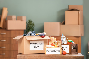 Donation boxes with food products and clothes on table indoors