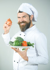 Male chef in cook uniform with smile holds onion in hand. Cooking and vegetarian diet concept. Chef presenting healthy food vegetarian salad isolated on white background. Cooking process concept.