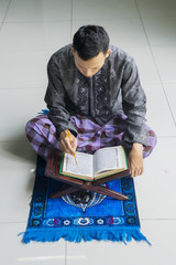 Fototapeta na wymiar Male muslim reads Quran on the mat