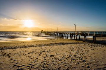 Fototapeta premium Beautiful colorful sunset summer view to the calm great ocean with pure sandy beach and a lovely empty wooden jetty lighten the night at a public boulevard, Glenelg Jetty, Adelaide, South/ Australia