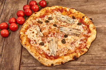 Homemade fresh delicious gourmet pizza Romana whit anchovies,capers and oregano,Tasty italian pizza isolated on wooden table, close up