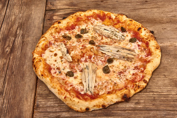 Homemade fresh delicious gourmet pizza Romana whit anchovies,capers and oregano,Tasty italian pizza isolated on wooden table, close up
