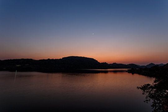 Amazing twilight. The lake is waiting for nightfall. The sun has set by the mountain. Multicolored sky. Silhouettes of mountains. The first stars are lit. New moon.India. Hampi. Magical lake. © mishamif