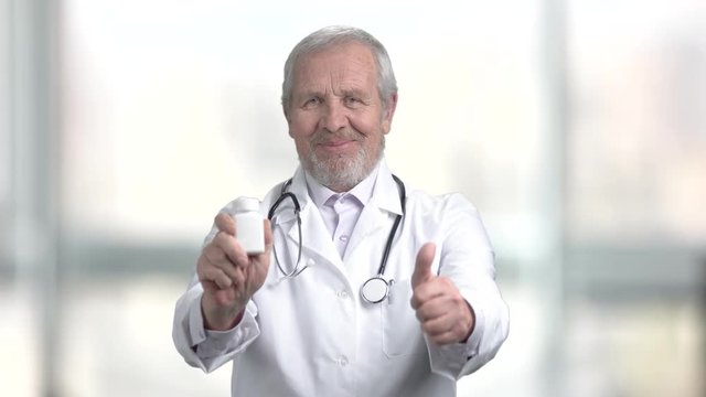 Aged doctor holding bottle with pills. Senior male doctor with pills showing thumb up. New effective medical product.