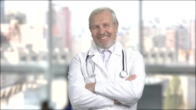 Joyful mature doctor, portrait. Happy senior doctor folded arms standing on window city background. People, professions, emotions.