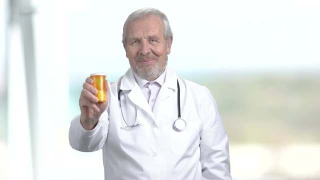 Smiling doctor with pills, portrait. Elderly doctor holding pills, gesturing thumb up and looking at camera. Success in treatment.