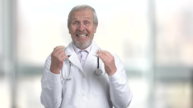 Happy surprised senior doctor, portrait. Joyful medical worker clapping hands on blurred background. Human gestures and emotions.