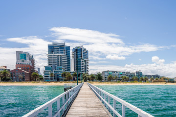 Fototapeta premium Port Melbourne, Victoria, Australia: piękne słoneczne wybrzeże z widokiem na australijskie błękitne morze i port przy plaży ze statkiem wycieczkowym Sprit of Tasmania na brzegu i molo mewy białej do zatoki na plaży
