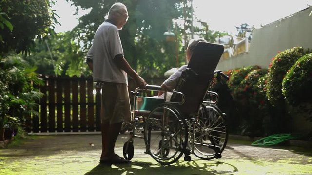 Happy elderly man talking with his paralyzed wife on wheelchair while sunbathing for health at home