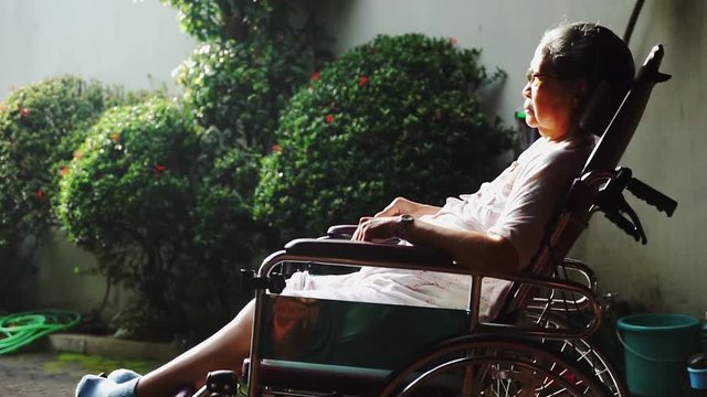 Elderly woman with paralysis disease sitting on wheelchair while sunbathing for health on the morning at home