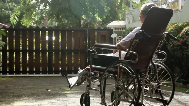 Lonely paralyzed elderly woman sitting on wheelchair while sunbathing for health on the morning at home
