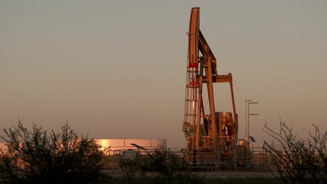 UHD Nodding donkey at sunset with gas tank in background