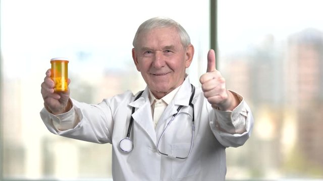 Physician is advising to use antidepressants. Old doctor in white coat and stethoscope consulting and recommed vitamins. Blurred city background out of window.