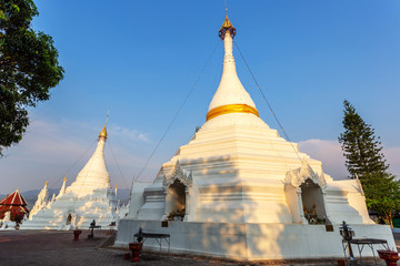 Golden light shining on white and gold pagoda during sunrise / sunset with blue sky in Mae hong son Thailand