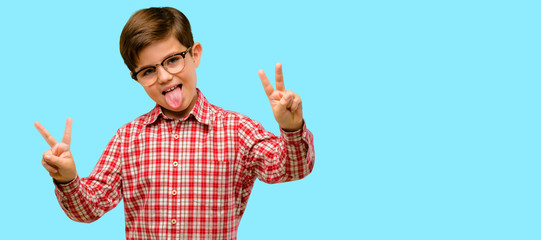 Handsome toddler child with green eyes looking at camera showing tong and making victory sign with fingers over blue background