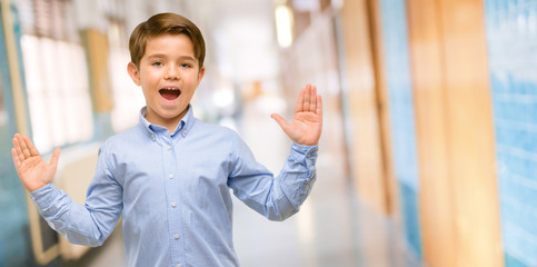 Handsome toddler child with green eyes happy and surprised cheering expressing wow gesture at school corridor