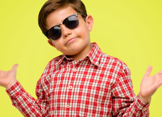 Naklejka premium Handsome toddler child with green eyes doubt expression, confuse and wonder concept, uncertain future over yellow background