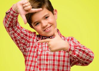 Handsome toddler child with green eyes confident and happy showing hands to camera, composing and framing gesture over yellow background