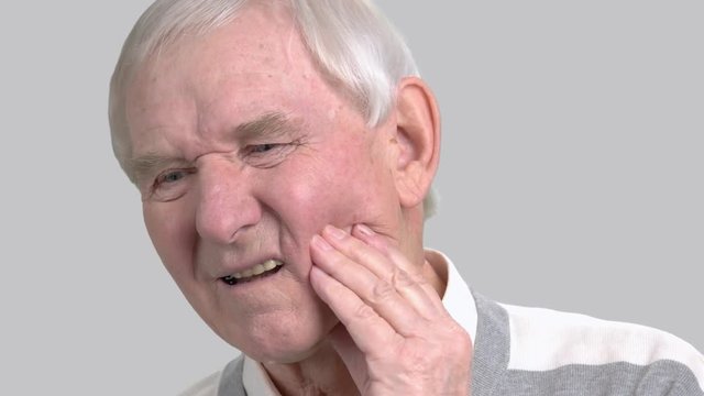 Older man with the tooth pain, toothache. Male senior suffering from terrible toothache on grey background. Sick old man.