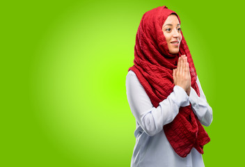 Young arab woman wearing hijab with hands together in praying gesture, expressing hope and please concept