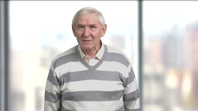 Emotional angry pensioner, blurred background. Stressed irritated ederly man is arguing pointing with finger. Facial expression of disappointment.