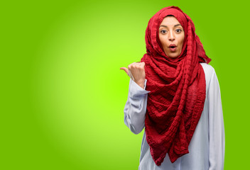 Young arab woman wearing hijab happy and surprised cheering expressing wow gesture pointing up