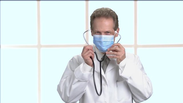 Stethoscope being in use by mature friendly doctor. Doctor hold stethoscope use for patient who come to make health check up. Big bright checkered framed windows background.