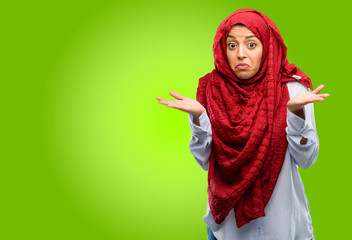 Young arab woman wearing hijab doubt expression, confuse and wonder concept, uncertain future shrugging shoulders