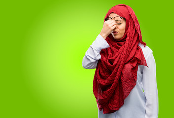 Young arab woman wearing hijab with sleepy expression, being overworked and tired, rubbes nose because of weariness