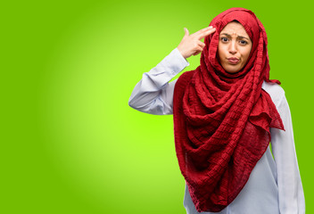 Portrait of woman in hijab making suicide gesture against green background